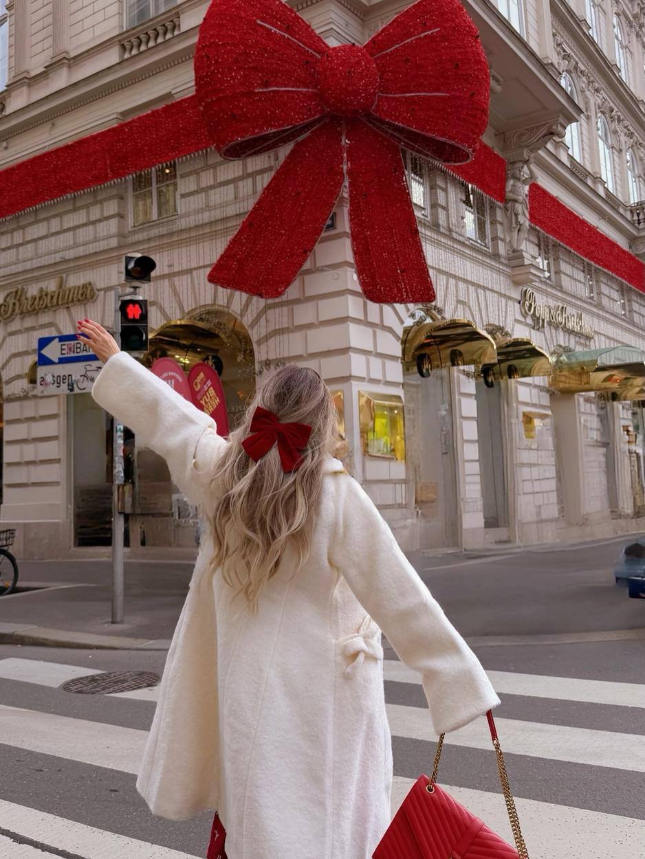 Pearla waving beneath a giant red bow on a Vienna street